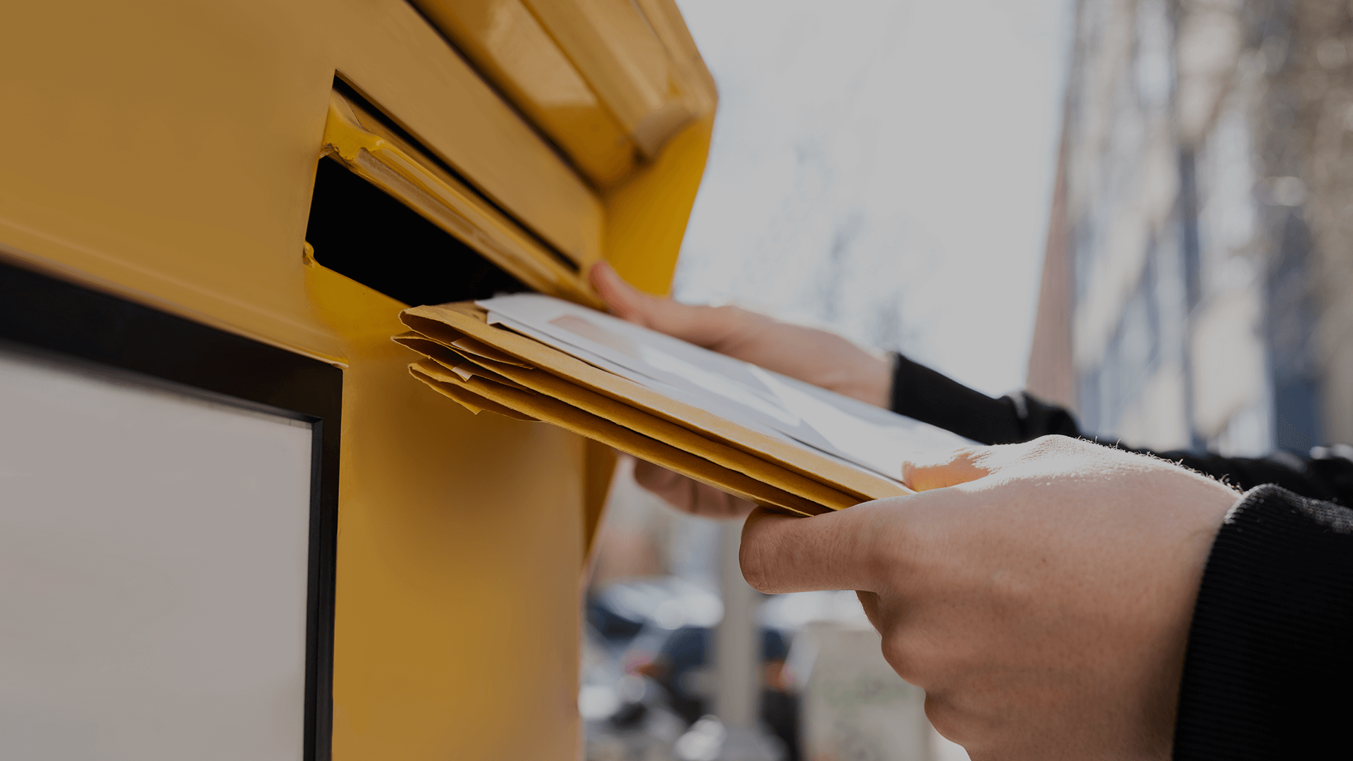 A person putting mail into a yellow postbox